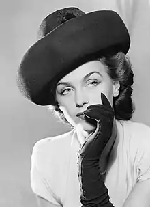 Fashion portrait photography of Genberg. She is looking away from the camera, wearing a hat, and her left hand which is gloved is by her face.