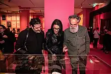 Three people look at a glass display case in an exhibition. They are smiling and gesturing to each other.