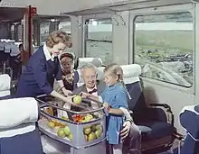 A young lady delightfully accepting an apple given to her by a train waitress
