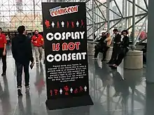 Tall black standing sign with the phrase "Cosplay Is Not Consent" in large lettering, alongside New York Comic Con branding and further explanatory text in smaller lettering.