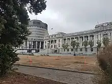 A pathway and soil where there was once lawn with New Zealand's Parliament buildings in the background framed by trees
