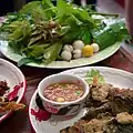 Yellow and white makhuea pro (Thai eggplant) in the background, fritters made from makhuea muang (purple eggplant) in the foreground, served with nam phrik kapi, a chili paste containing makhuea phuang (Thai pea-sized eggplants)