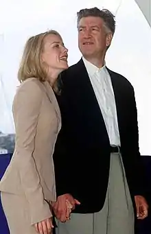 A blonde woman and a grey-haired man, holding hands and smiling