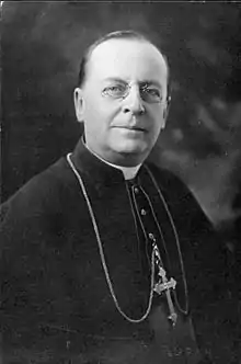A bespectacled man wearing a mozzetta and pectoral cross faces forward.