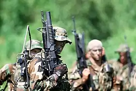 The U.S. Navy SEAL in the foreground is carrying a field radio and is armed with a Colt Model 653 carbine equipped with an M203 grenade launcher.