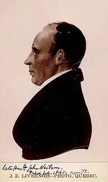 Left profile of a light-skinned man, balding dark hair, wearing a dark suit