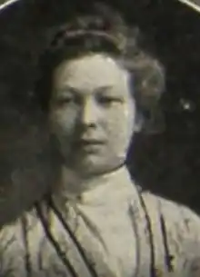 A young white woman, wearing a high-collared blouse with ribbon trim