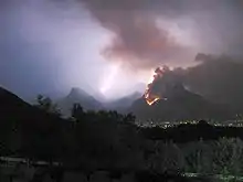Mountain on fire in the night, with lightning striking in the background.