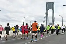 Three runners in a race down a street where onlookers are cheering behind barriers.