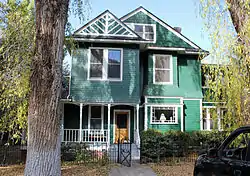 A green wooden house with white trim and two pointed roofs.