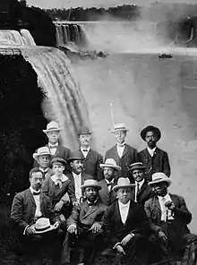 A dozen African American men seated with Niagara Falls in the background