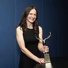 Nicole Dubuc smiling while holding her Writers Guild Award with her left hand