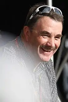 Nigel Mansell with a pair of sunglasses atop his head and sporting a moustache