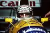 Nigel Mansell wearing a crash helmet with sponsors logos and sitting inside a blue, yellow and white racing car