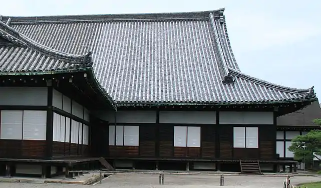 On the right, three grooves, three panels. The maira-do are open, and the single shōji panel closed; half of the area is still filled with the maira-do. The building to the left is newer; its outer groove runs outside the pillars. The shutters are packed away in the to-bukuro in the corner, and the shōji in the inner two grooves run uninterrupted.