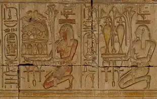 Relief showing two kneeling people carrying trays piled with plants, jars of liquid, and food