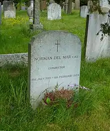 A granite headstone inscribed with a cross, in a grassy churchyard