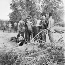 A number of Asian men wearing blindfolds are standing while a number of caucasian soldiers stand behind them.