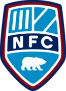 A shield with the letters "NFC" in the middle and the remainder divided into three sections, the top left corner containing three white stripes and the top right two white stripes. In the bottom section is a polar bear rearing on all fours. All on a blue background