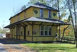 Old but well-refurbished yellow building with black tiling and siding. A sign on the side of the building facing the camera reads "BUCKINGHAM TOWNSHIP MUNICIPAL BUILDING." There is a small post with a map of Wayne County, Pennsylvania attached to it on the same side of the building.