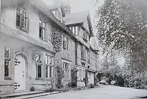 Large country house by river with wooded hillside beyond- 1900 postcard