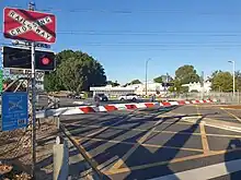 Railway level crossing with boom gates blocking the road and a sign with red flashing lights indicating a train will be coming through