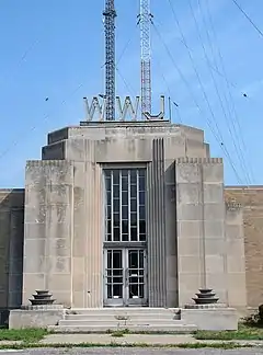 A white stone building with letters WWJ above it, and behind it, two broadcast towers are visible, one gray and one red and white
