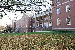 The front of Delano Hall, a three-story brick building that houses the District of Columbia International School, with grass and fall leaves in front.