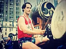 A marathon runner with a red shirt playing taiko drums after finishing the marathon