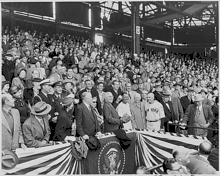 A wide shot with United States president Harry Truman in the center throwing a baseball.