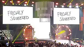 A color photograph of a stage with two screens that say "Freshly Squeezed"