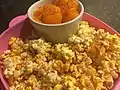 Mandarin oranges in a bowl within a bowl of popcorn, both sprinkled in Tajín powdered seasoning