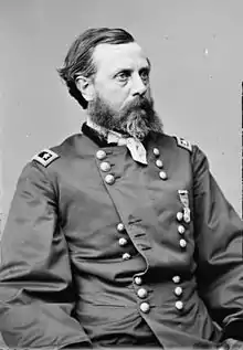 Black and white photo shows a man with dark hair and a beard. He wears a dark military uniform with the shoulder tabs of a major general (two stars).