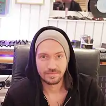 A man wearing a grey beanie and a black hoodie while sitting in a music studio.