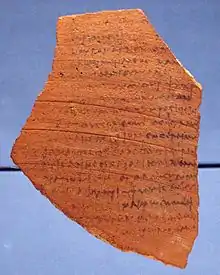 A fragment of teracotta pottery, written on with black ink.