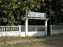A white gate with a sign reading "Republique du Senegal: Prefecture d'Oussouye"