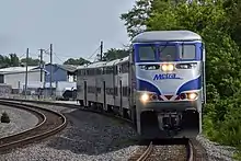 An outbound North Central Service train approaches Schiller Park station in June 2019, being led by an Ex-Amtrak EMD F59PHI