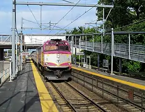 A purple and silver passenger train with a diesel locomotive arriving at a station