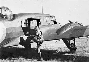 Rear three-quarter view of twin-engined military aircraft, being boarded by a man in flying gear