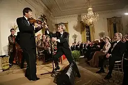Shoji Tabuchi performing at the White House for an audience that includes George W. Bush. The prime minister of Japan Junichiro Koizumi is holding the microphone stand for him with both hands.