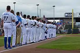 Men in mostly white baseball uniforms lined up on baseball field's foul line