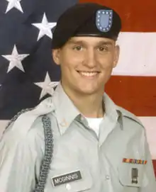 Head and shoulders of a smiling young man in circa 2000 U.S. Army uniform with beret, before a large American flag.