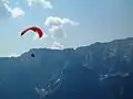 Note kite's wing and many kite lines held by human operator; operator moves by gravity (paraglider kite system)