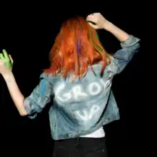 An image of Hayley Williams from behind wearing a denim jacket that reads "GROW UP" in white