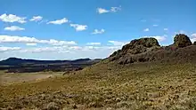 Small, rocky hills interspersed above a flat landscape with bushes