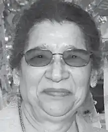 A smiling older South Asian woman wearing tinted glasses
