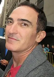 A 49-year old, dark-haired man, smirking into the camera.