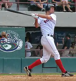 A man in a white baseball uniform and red socks swings left-handed at a baseball.