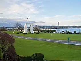 A white stone arch in a grassy lawn in front of a line of automobiles