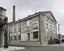 A two-story industrial stone building with various façade layers